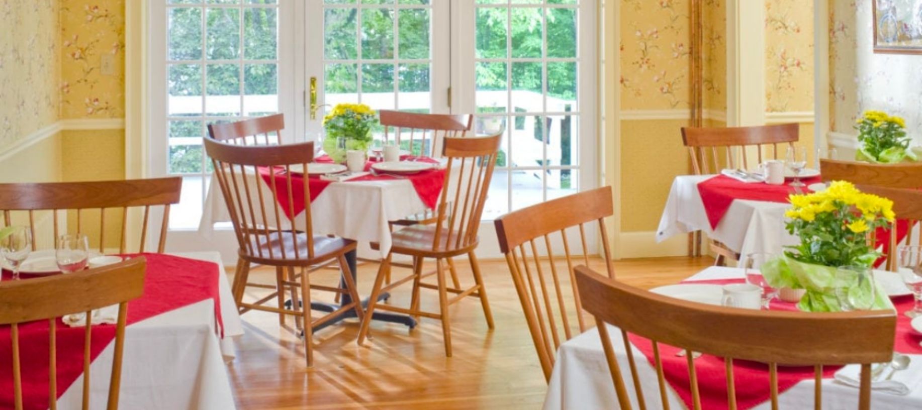 Cheery yellow dining room with red table cloths and lots of windows