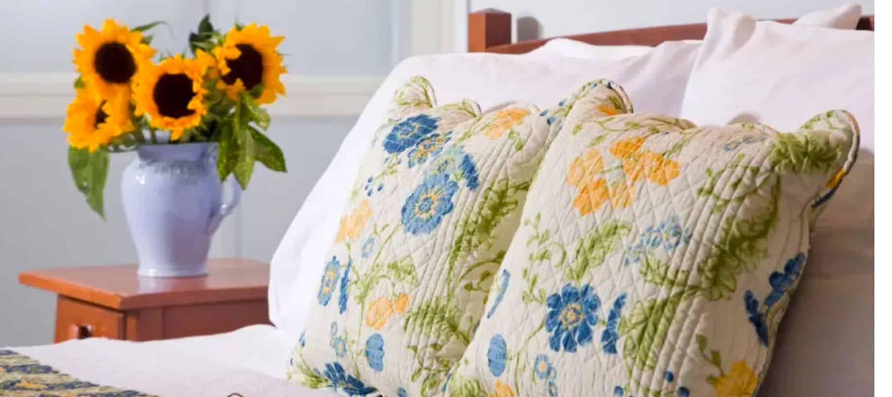 Guest bed with yellow and blue floral bedding, plump pillows and fresh sunflowers