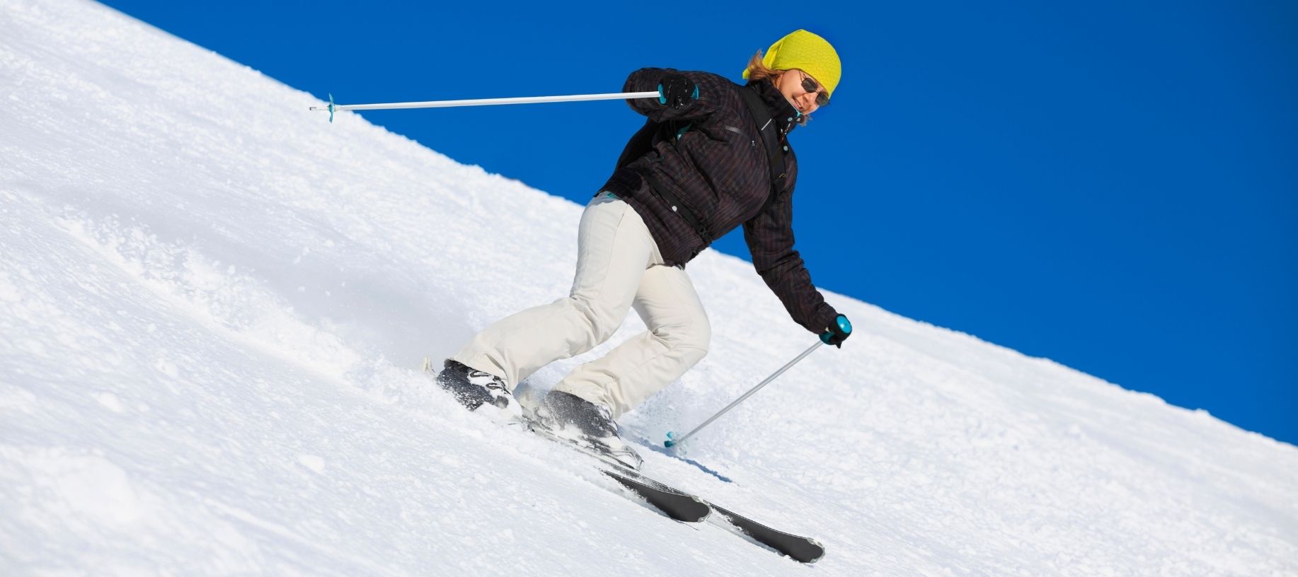 Woman snow skiing down a hill amidst blue skies