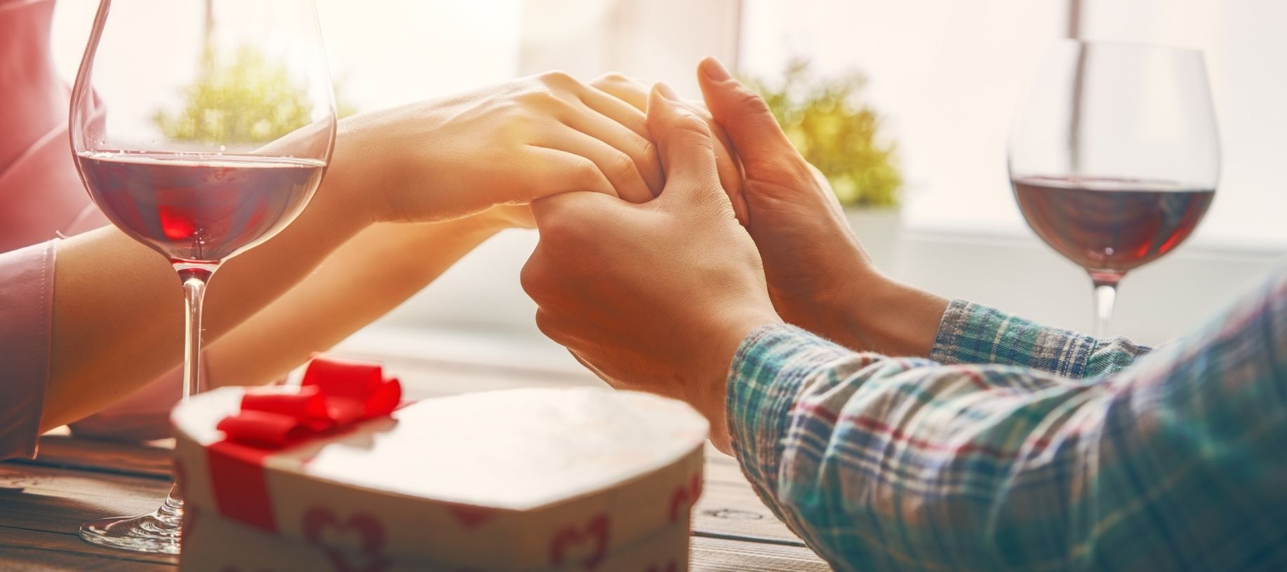 Couple holding hands over dinner with red wine and heart-shaped box