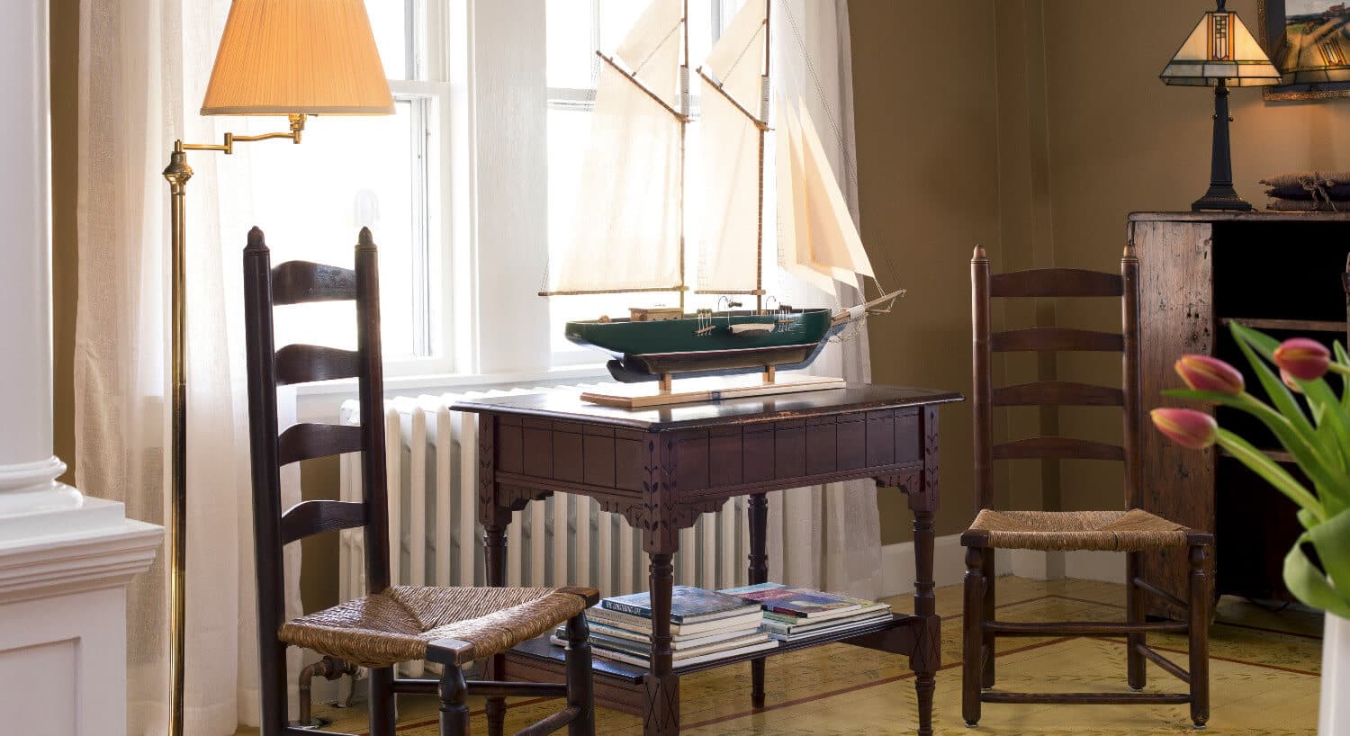 Sitting area in parlor with two wooden chairs an a model ship on a small table.