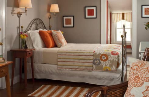 Clean and fresh bedroom decorated in grey and orange with a large brass bed and comfortable seating.