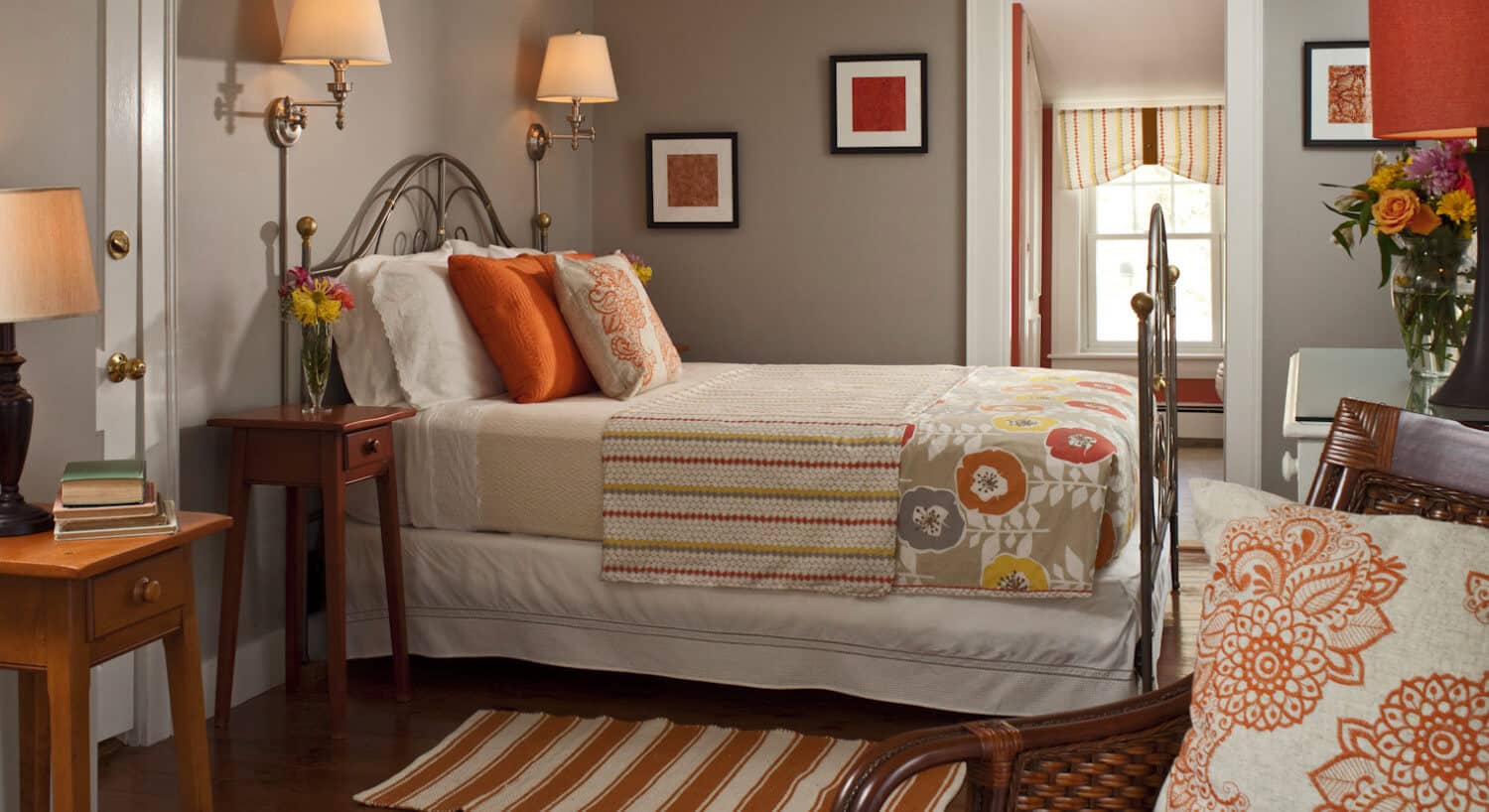 Clean and fresh bedroom decorated in grey and orange with a large brass bed and comfortable seating. 