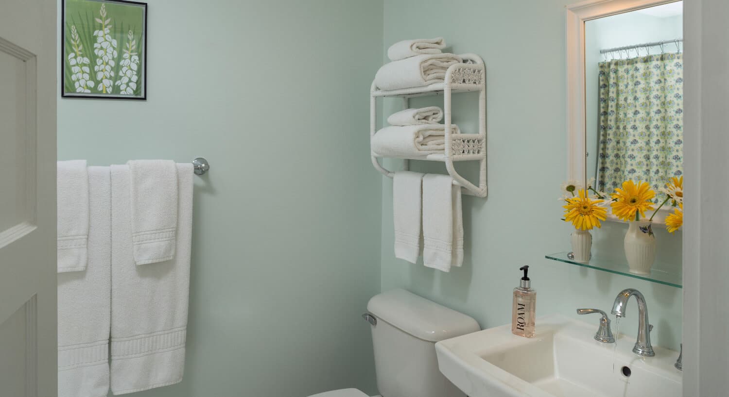 Bathroom with pale green walls, a pedestal sink, stool and towel racks. 