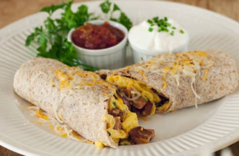 Breakfast burrito with eggs and bacon, garnished with salsa and sour cream.