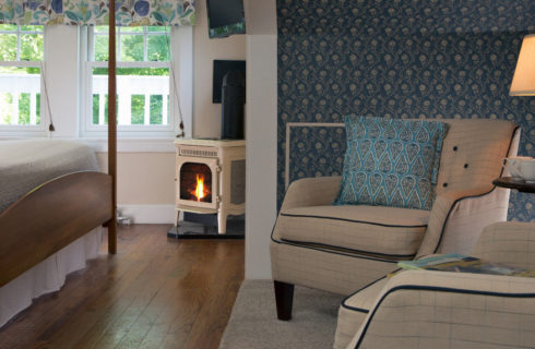 Bedroom with blue wallpaper, comfortable armchairs and a small gas stove.