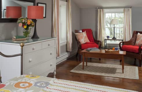 View of seating area in bedroom from the bed, including a white dresser topped with a lamp.