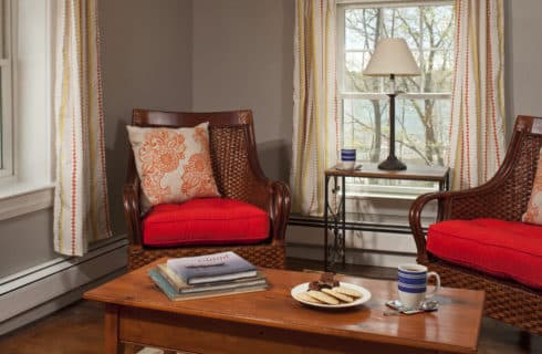 Wooden armchairs with red cushions forma seatign area with a wooden side table and coffee table.