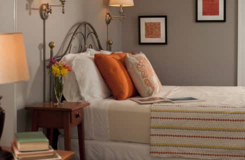Clean and fresh bedroom decorated in grey and orange with a large brass bed and comfortable seating.