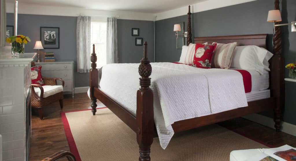 Large four-post bed made up in white in a room with grey walls and white crown molding.