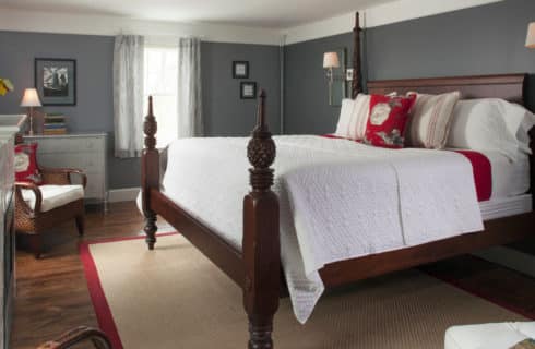 Large four-post bed made up in white in a room with grey walls and white crown molding.