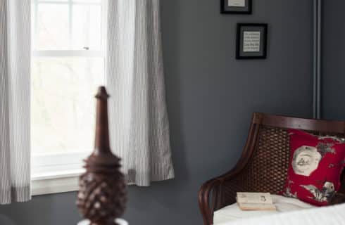 Detail of pineapple bed post next to a large window and wicker chair in the corner of the room.