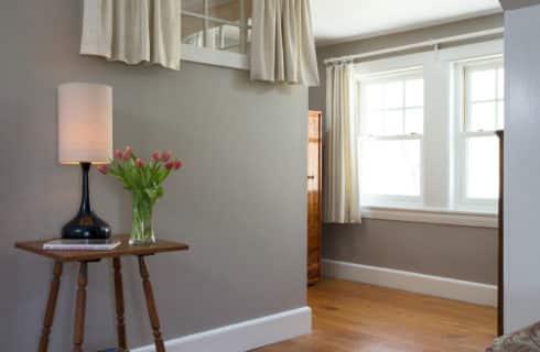 Detail of a table with a lamo in the bedroom painted grey with wood floors.