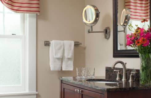 Bathroom with a large window, a dark wood vanity and mirror and beige walls.