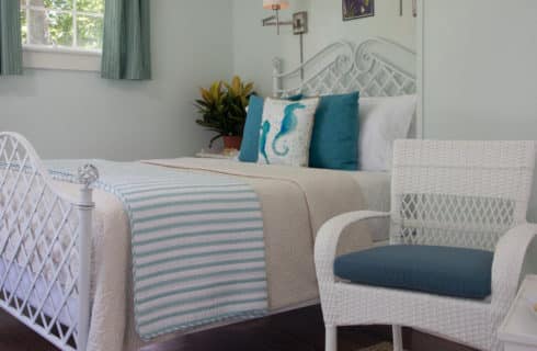 Clean and bright bedroom with pale painted walls and a white bed made up in blue striped bedding with a small seating area in white.