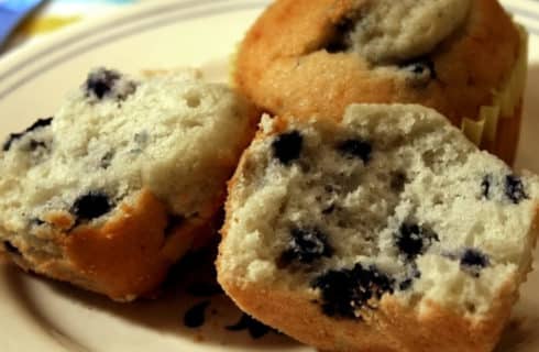 Blueberries muffins on a yellow plate with one cracked open.