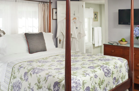 Bedroom painted in pale lavender with a cherry four-post bed made up in a lavender patterned cover with a cherry dresser.