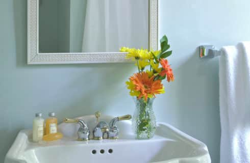 White pedestal sink with yellow and orange flowers in a vase topped with a white-framed mirror.