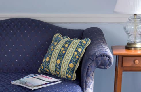 Blue coouch with decorative pillows next to a side table with a lamp.