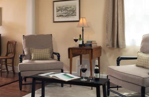 Two beige armchairs are joined by an end table with a lamp and a coffee table in a relaxing sitting area.