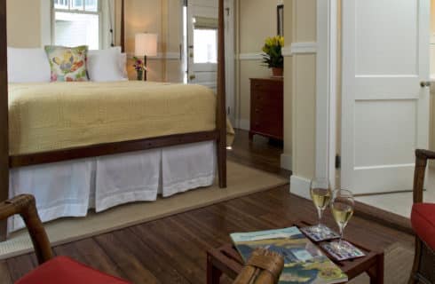 Wooden four-posted bed made up with a gold spread in a room painted beige with white chair rail and wooden floors.