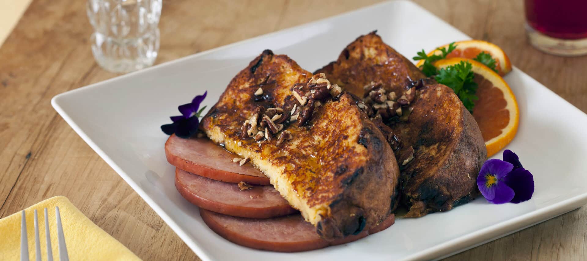 French toast on a white plate with ham and garnished with orange slices.