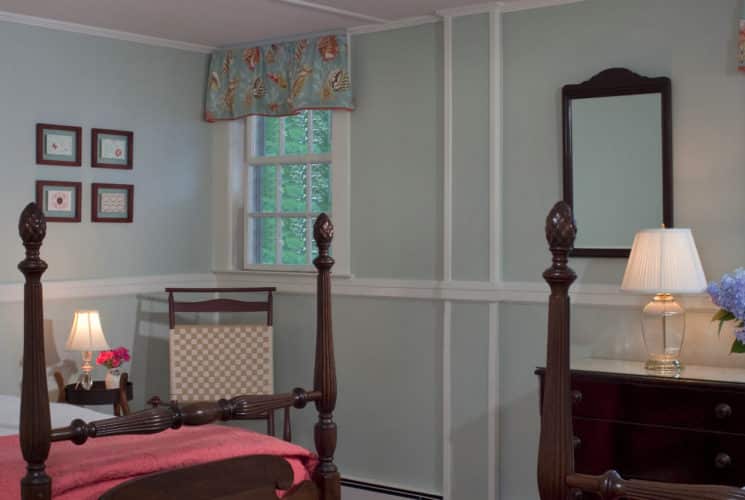 Cozy bedroom with wooden four-post bed made up in white and coral bedding with a dark wood dresser and mirror.