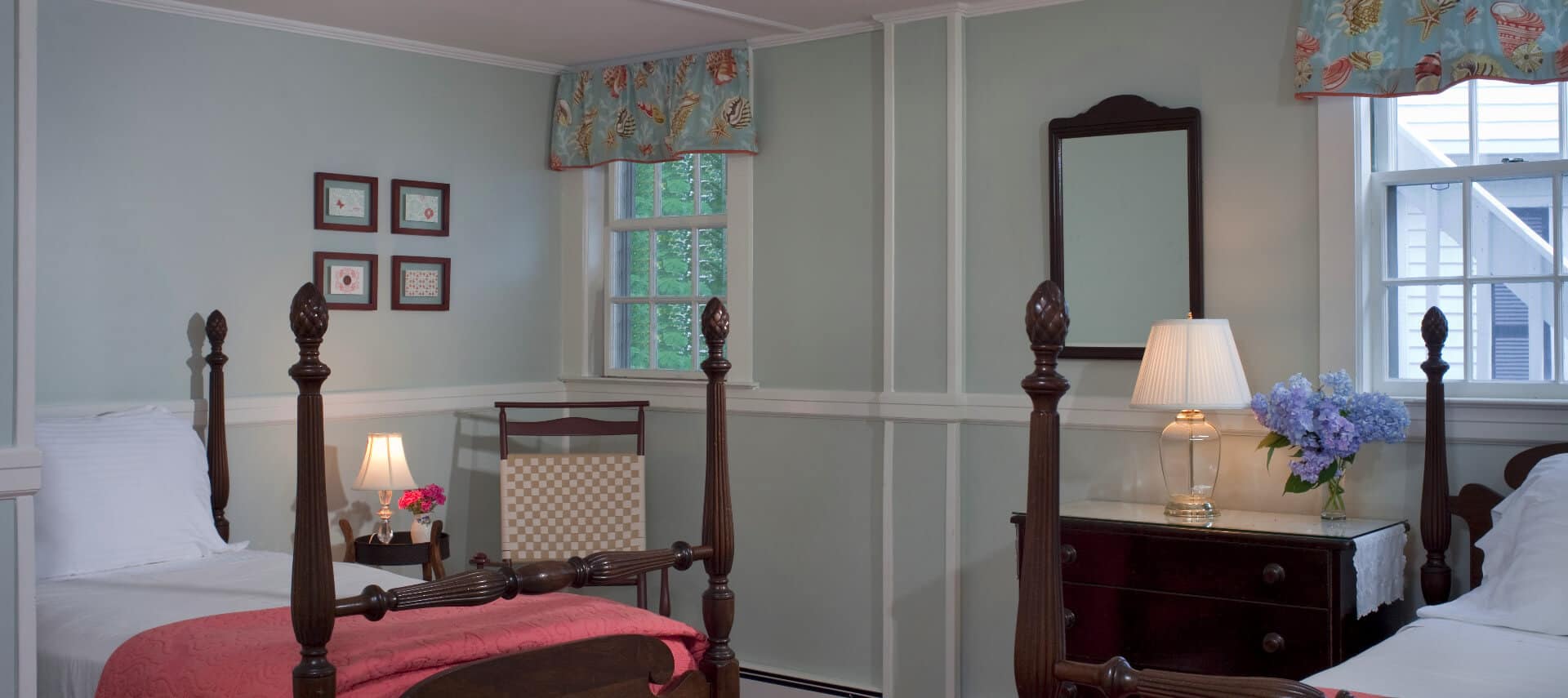 Cozy bedroom with wooden four-post bed made up in white and coral bedding with a dark wood dresser and mirror.