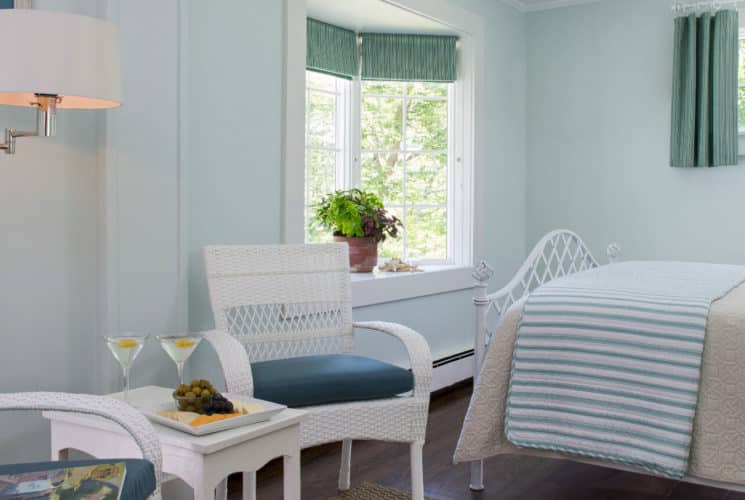 Clean and bright bedroom with pale painted walls and a white bed made up in blue striped bedding with a small seating area in white.