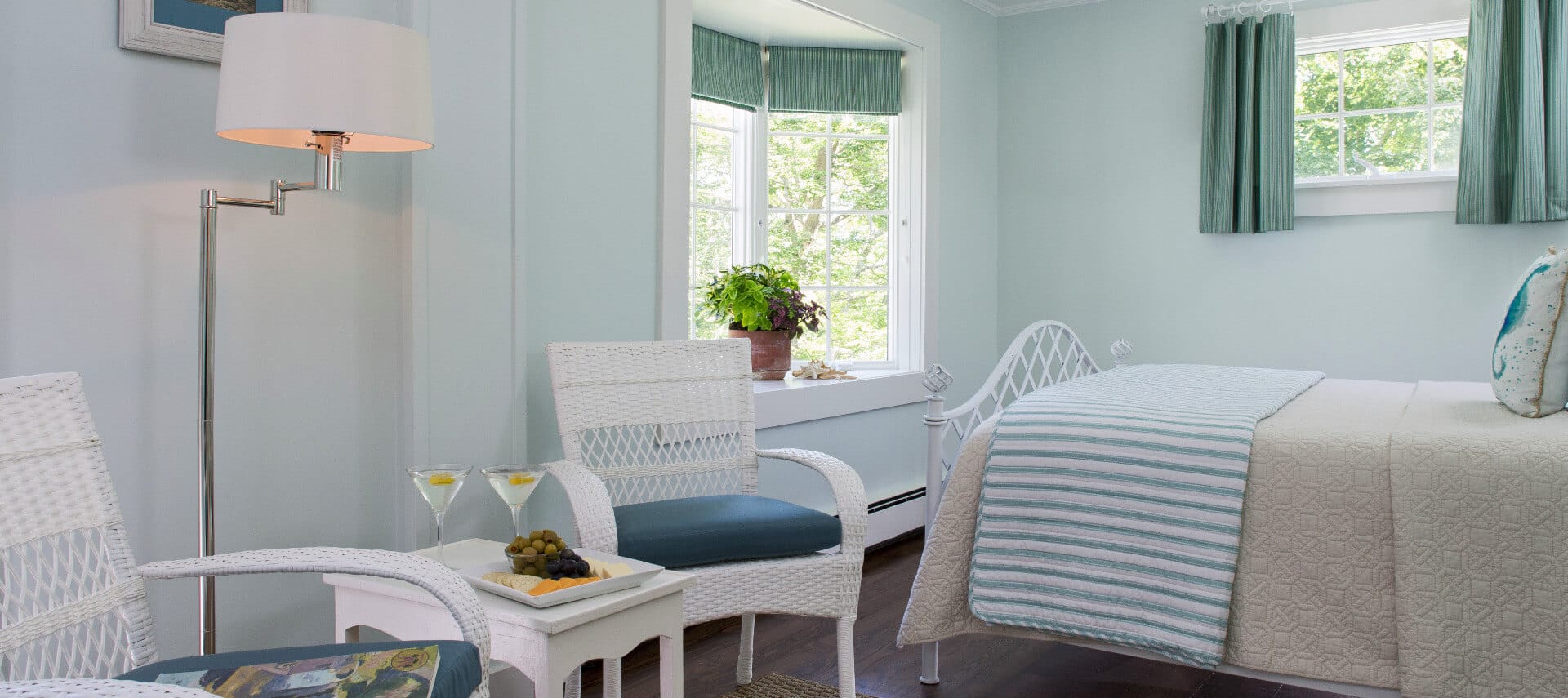 Clean and bright bedroom with pale painted walls and a white bed made up in blue striped bedding with a small seating area in white.