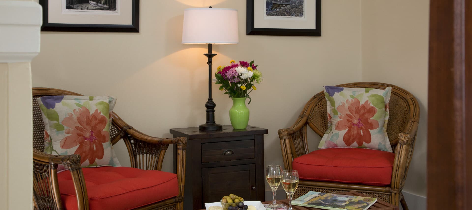 Two wicker chairs with red cushions and flowered pillow form a seating area with an end table and a coffee table.