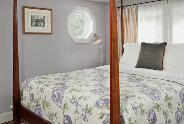 Bedroom painted in pale lavender with a cherry four-post bed made up in a lavender patterned cover.