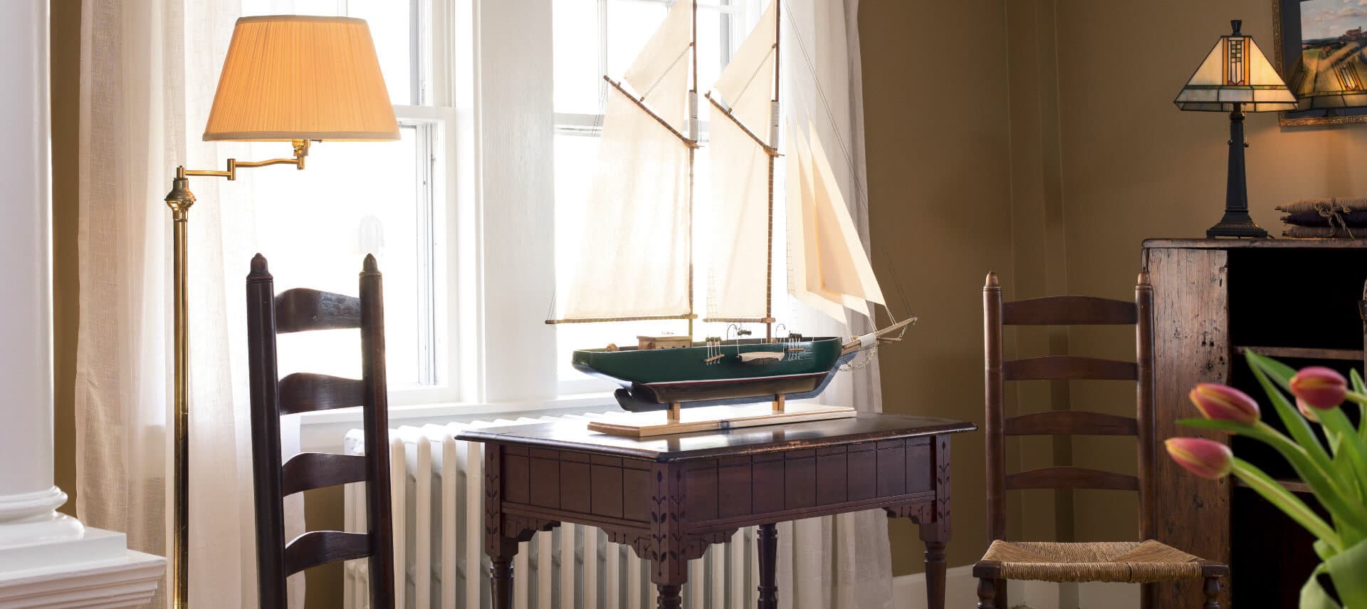 Sitting area in parlor with two wooden chairs an a model ship on a small table.