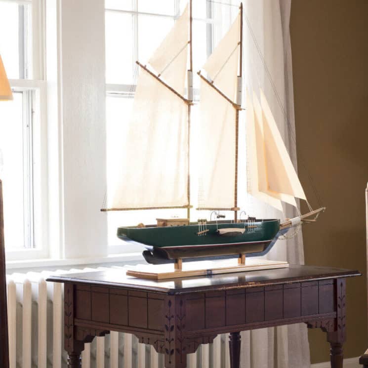 Sitting area in parlor with two wooden chairs an a model ship on a small table.