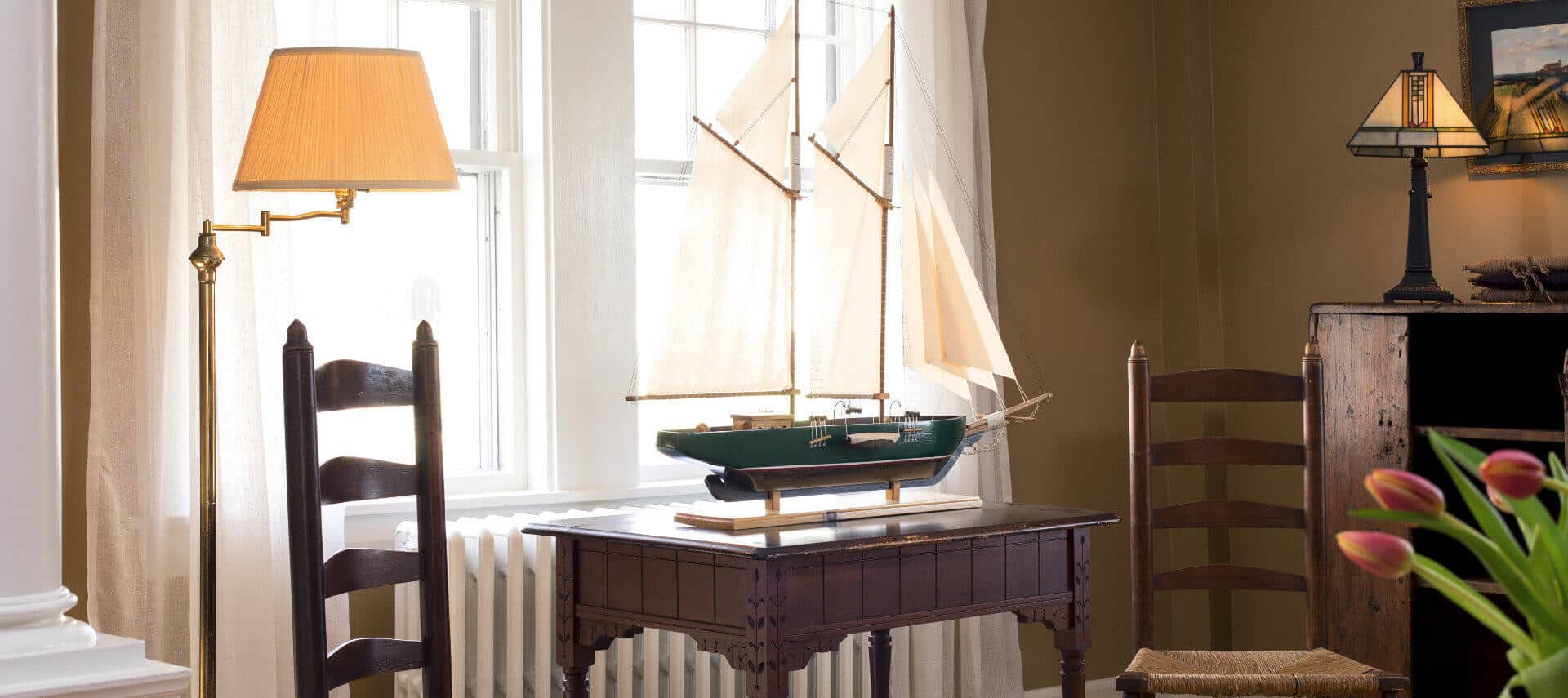 Sitting area in parlor with two wooden chairs an a model ship on a small table.