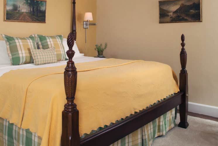 Large four-post wooden bed made up in clean linens in a roomw ith pale painted walls.