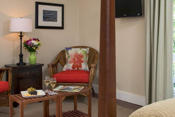 Wicker chairs with red cushions form a seating area with a small table n the corner of a bedroom.