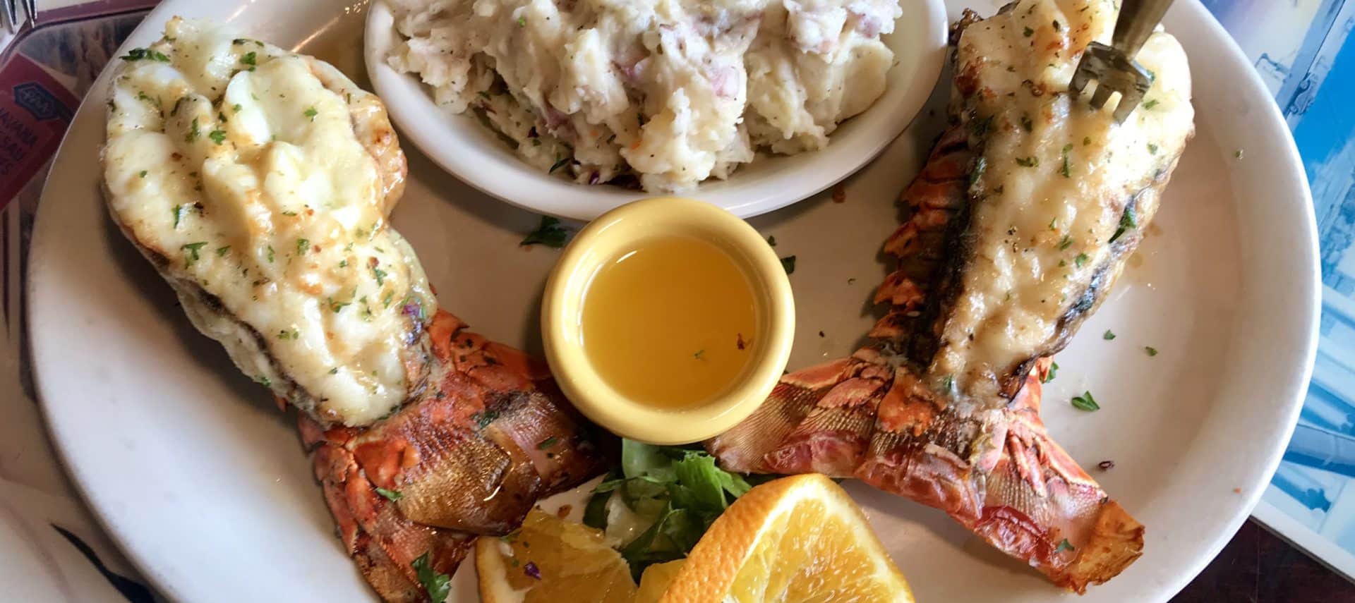 white plate topped with fresh cooked lobster, mashed potatoes, and dipping sauce