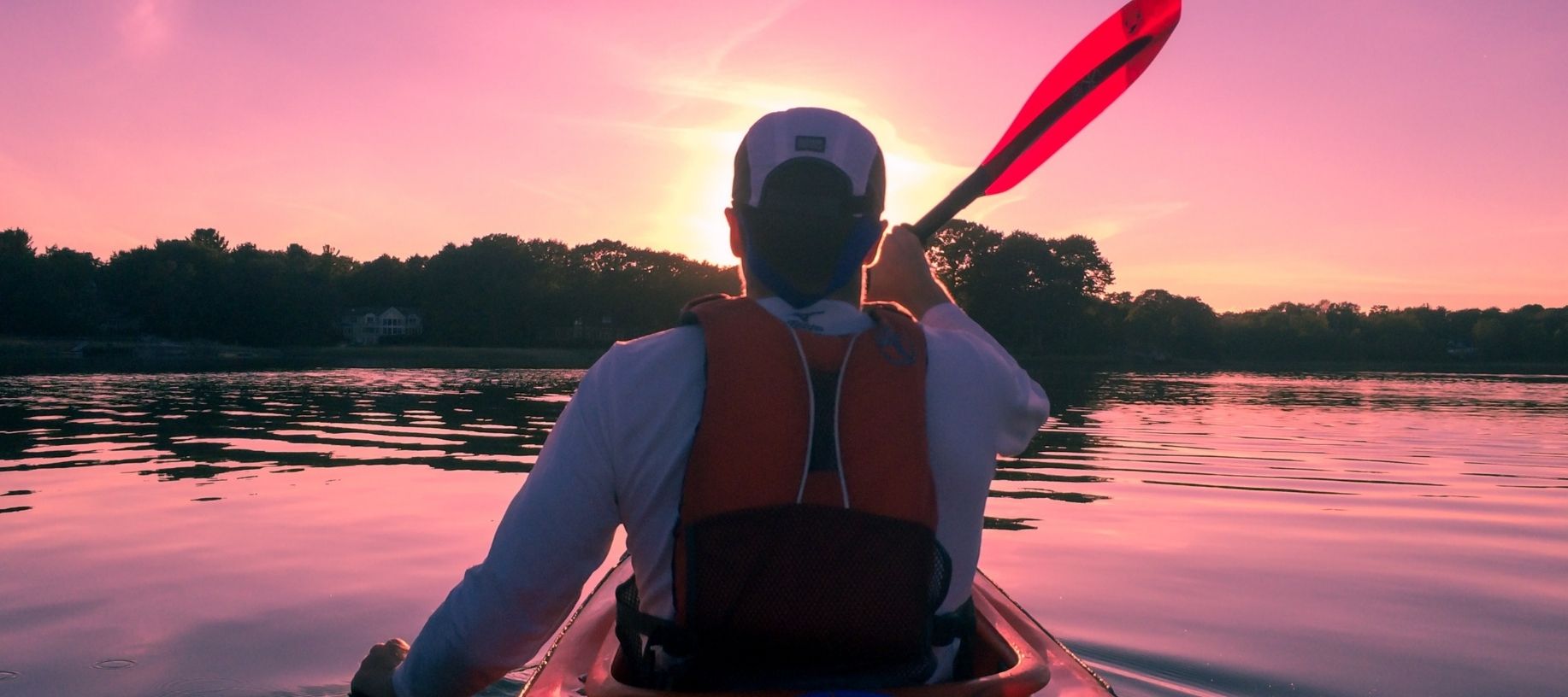 Man rowing a kayak in the early morning with a pink dawn sky