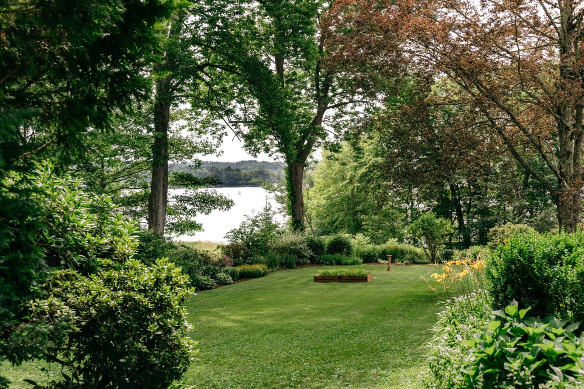 Two white adirondack chairs next to a small table on the grass overlooking the water.