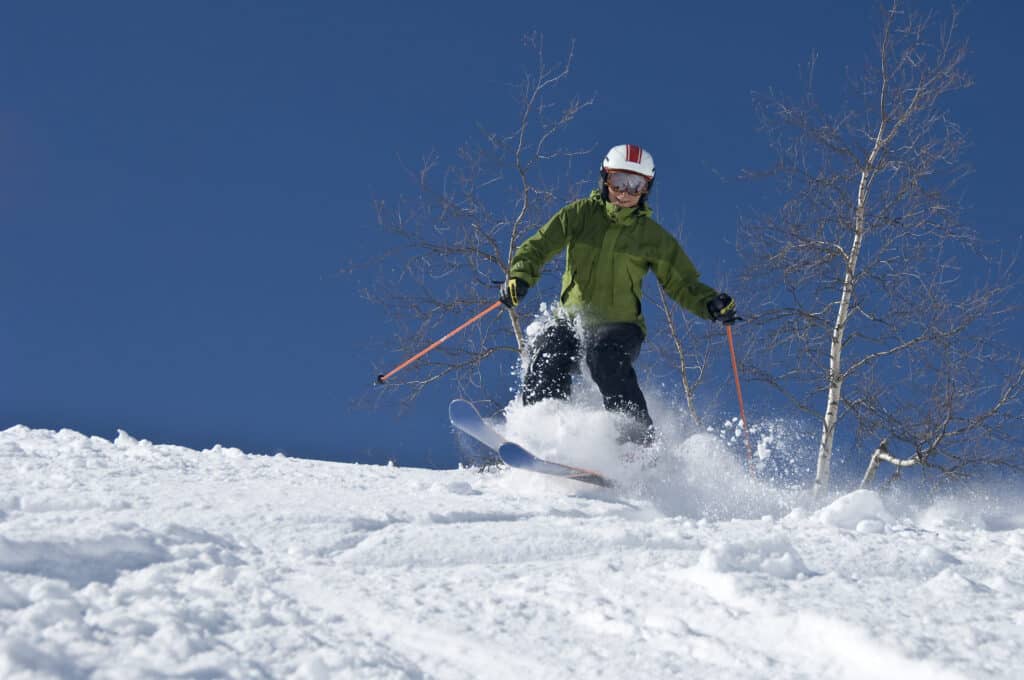 person in green parka skiing down a mountain against a blue sky